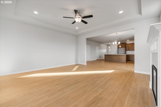 unfurnished living room with a tray ceiling, ceiling fan with notable chandelier, and light hardwood / wood-style floors