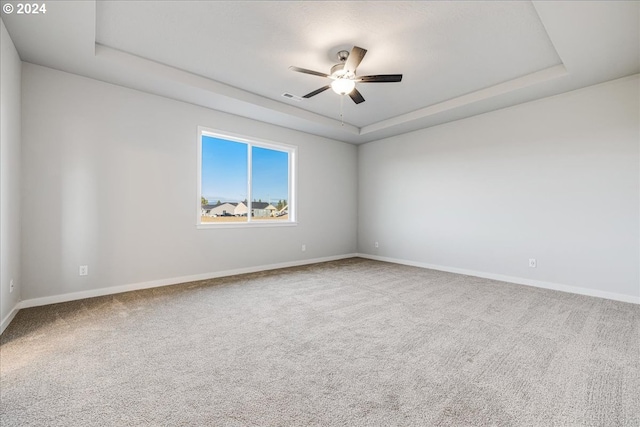 carpeted spare room featuring ceiling fan and a raised ceiling