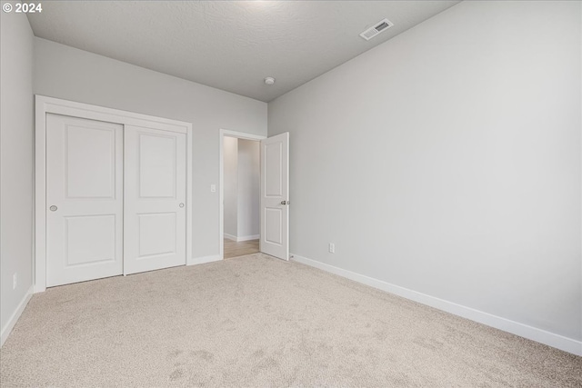 unfurnished bedroom with a textured ceiling, light colored carpet, and a closet