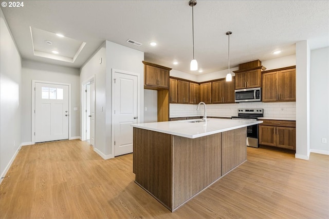 kitchen featuring tasteful backsplash, a kitchen island with sink, sink, light hardwood / wood-style floors, and stainless steel appliances