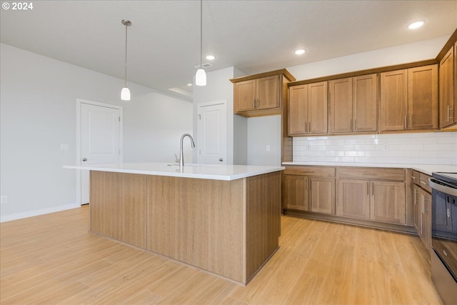 kitchen with black range with electric cooktop, backsplash, decorative light fixtures, light hardwood / wood-style flooring, and a center island with sink