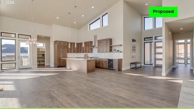 kitchen with a kitchen island with sink, decorative backsplash, wine cooler, decorative light fixtures, and wall chimney range hood