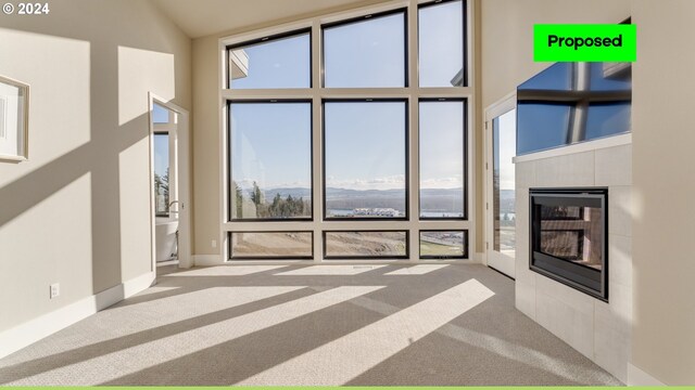 unfurnished living room with a wealth of natural light, light carpet, a tile fireplace, and a high ceiling