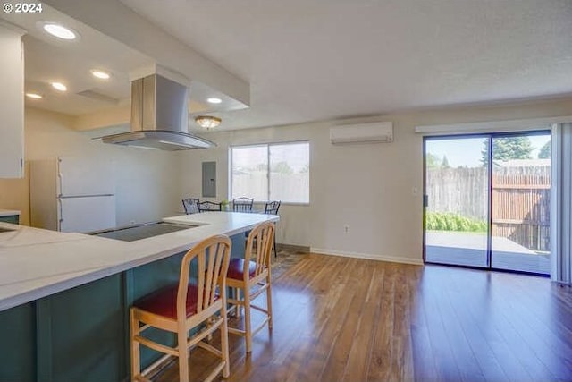 kitchen with wall chimney exhaust hood, a wall mounted air conditioner, black cooktop, hardwood / wood-style floors, and white fridge