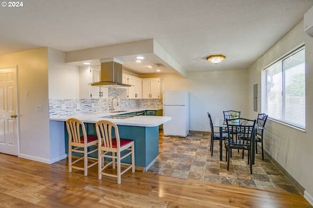 kitchen featuring kitchen peninsula, wall chimney range hood, hardwood / wood-style floors, white fridge, and white cabinetry