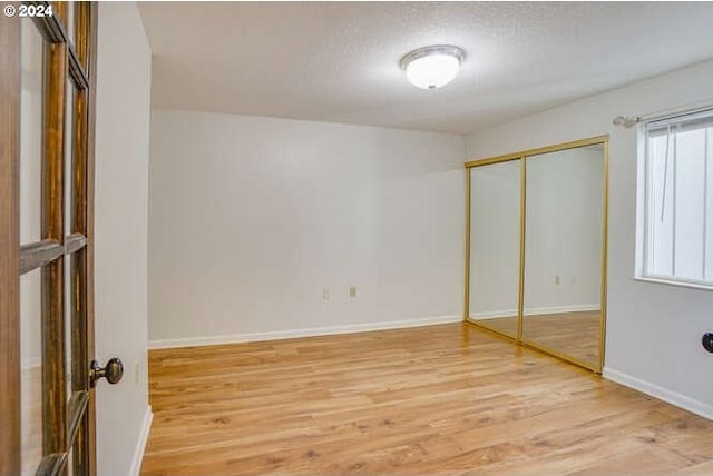 unfurnished bedroom with a textured ceiling, a closet, hardwood / wood-style flooring, and multiple windows