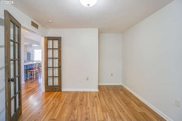 spare room with french doors, light wood-type flooring, and a textured ceiling