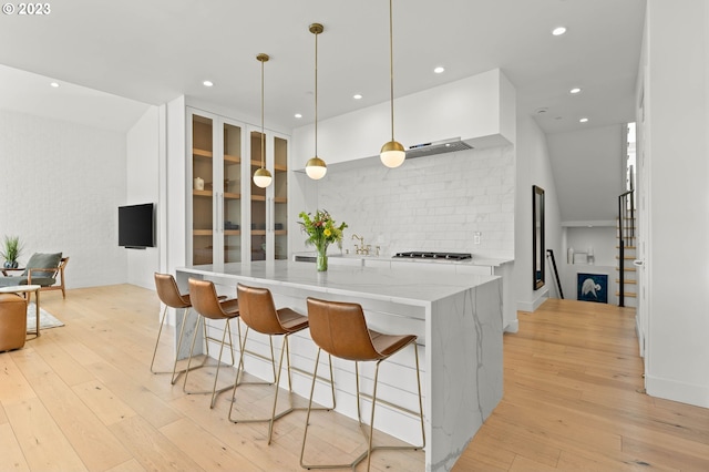 kitchen with stainless steel gas cooktop, light stone counters, light wood-type flooring, and pendant lighting