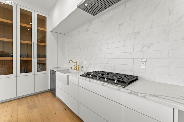 kitchen with light stone countertops, appliances with stainless steel finishes, backsplash, light hardwood / wood-style floors, and white cabinets