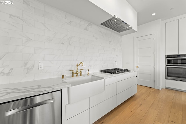 kitchen featuring tasteful backsplash, appliances with stainless steel finishes, light stone countertops, white cabinetry, and light hardwood / wood-style floors