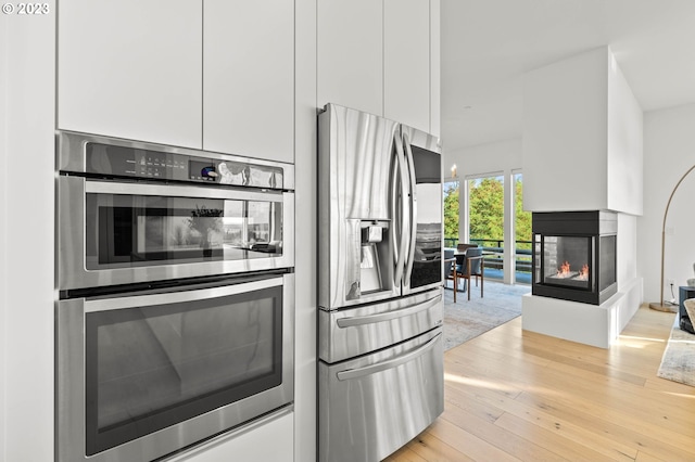 kitchen featuring appliances with stainless steel finishes, a multi sided fireplace, white cabinetry, and light hardwood / wood-style floors