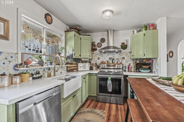 kitchen featuring stainless steel appliances, green cabinets, wall chimney range hood, and tasteful backsplash