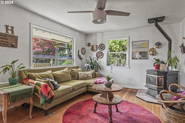 living room with a wood stove, ceiling fan, light wood-type flooring, and a textured ceiling