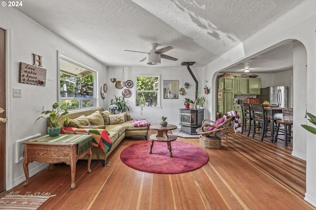 living room featuring a wood stove, a textured ceiling, hardwood / wood-style flooring, and ceiling fan