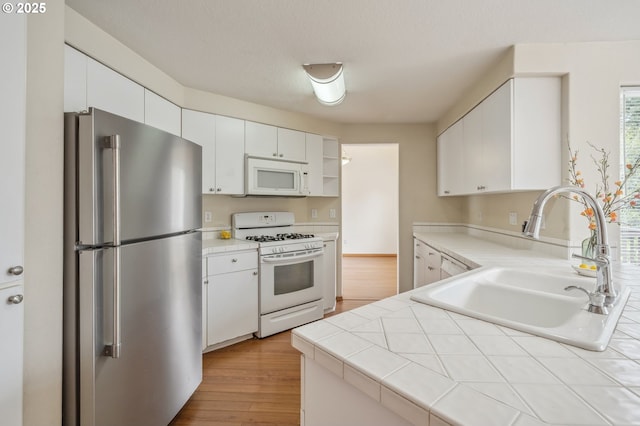4135 SW Brugger St, Portland, OR 97219 - kitchen with white appliances, tile countertops, white cabinets, and wood finished floors