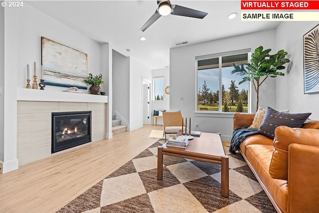 living room with wood-type flooring, a tile fireplace, and ceiling fan