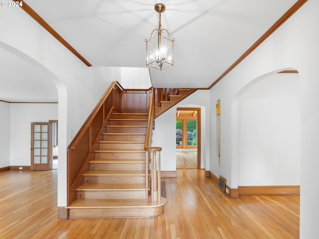 stairway featuring an inviting chandelier, crown molding, and wood-type flooring