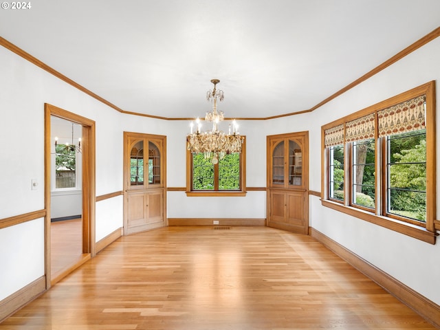 unfurnished dining area featuring light wood-type flooring, crown molding, and an inviting chandelier