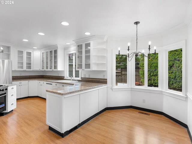 kitchen with pendant lighting, light hardwood / wood-style floors, light stone counters, kitchen peninsula, and stainless steel fridge