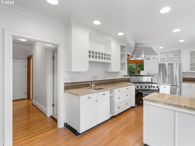 kitchen with wall chimney range hood, white cabinets, appliances with stainless steel finishes, light hardwood / wood-style floors, and sink