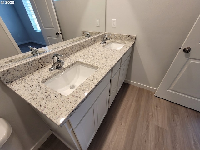 bathroom featuring double vanity, wood finished floors, a sink, and baseboards