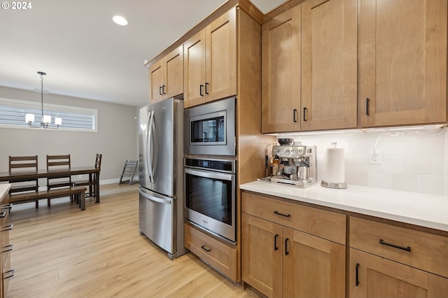 kitchen featuring tasteful backsplash, an inviting chandelier, light hardwood / wood-style flooring, pendant lighting, and stainless steel appliances