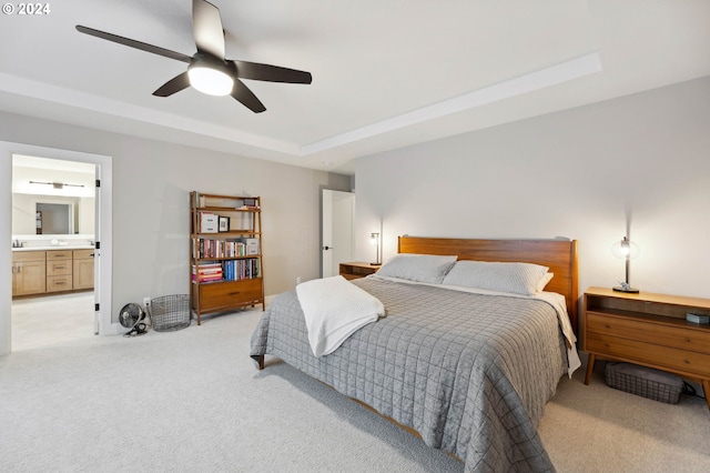 bedroom with connected bathroom, sink, light carpet, a raised ceiling, and ceiling fan