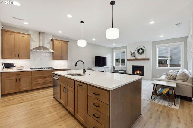 kitchen featuring sink, an island with sink, decorative light fixtures, wall chimney exhaust hood, and light wood-type flooring