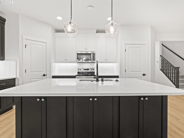 kitchen featuring a center island with sink, white cabinetry, light wood-type flooring, and stainless steel appliances