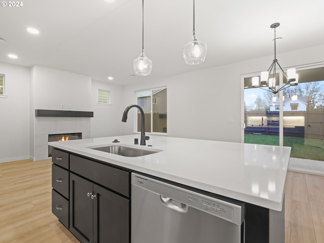 kitchen with a kitchen island with sink, sink, dishwasher, light hardwood / wood-style floors, and a tiled fireplace