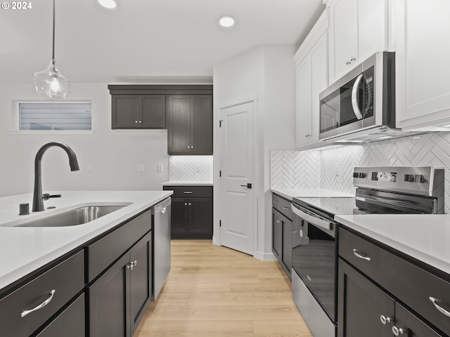 kitchen with light wood-type flooring, stainless steel appliances, sink, decorative light fixtures, and white cabinets