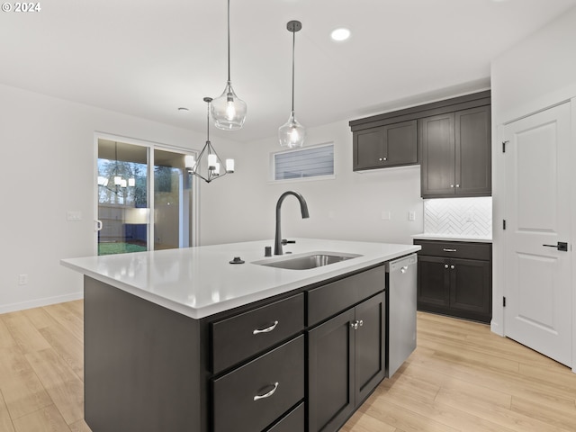 kitchen with sink, dishwasher, light hardwood / wood-style flooring, decorative light fixtures, and a kitchen island with sink