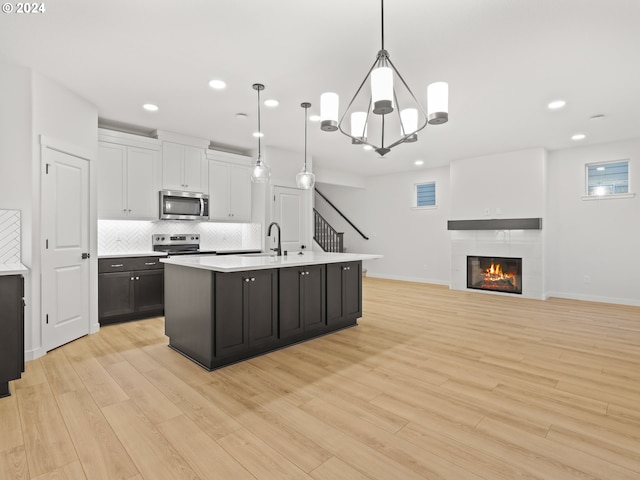 kitchen with appliances with stainless steel finishes, decorative light fixtures, light hardwood / wood-style flooring, and white cabinetry