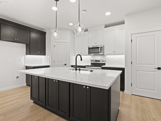 kitchen featuring hanging light fixtures, an island with sink, light hardwood / wood-style floors, white cabinetry, and stainless steel appliances