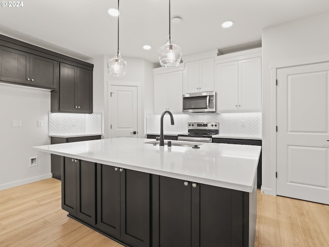 kitchen with an island with sink, stainless steel appliances, and light wood-type flooring