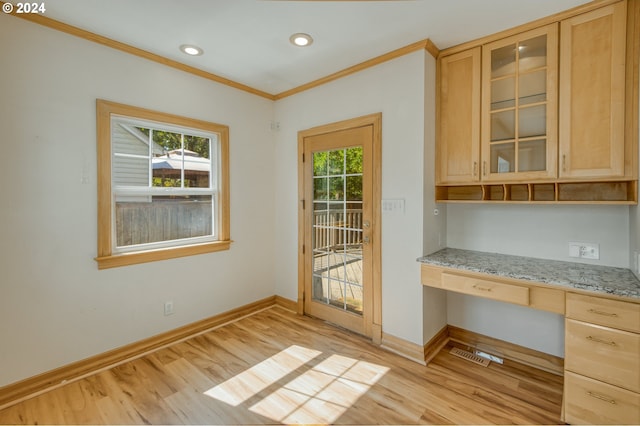 entryway with built in desk, ornamental molding, and light hardwood / wood-style flooring