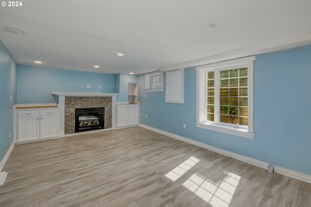 unfurnished living room featuring a stone fireplace and light hardwood / wood-style flooring