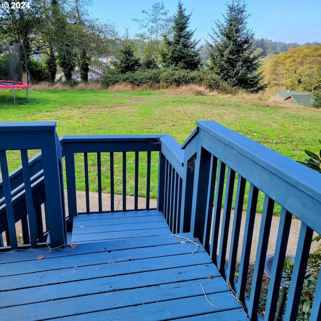 wooden terrace featuring a trampoline and a lawn