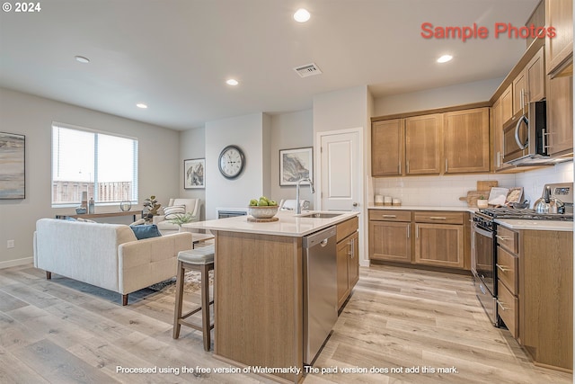 kitchen featuring an island with sink, sink, decorative backsplash, stainless steel appliances, and light hardwood / wood-style flooring