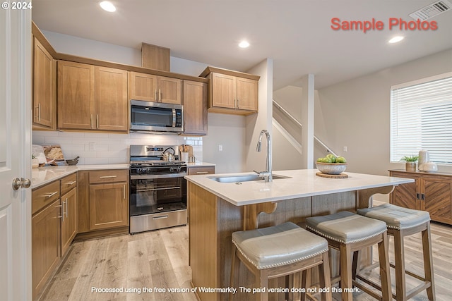 kitchen with appliances with stainless steel finishes, sink, a kitchen breakfast bar, a center island with sink, and light wood-type flooring