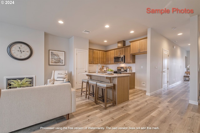 kitchen featuring sink, a breakfast bar area, a center island with sink, light wood-type flooring, and stainless steel appliances