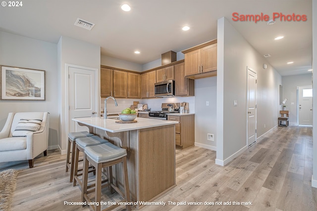 kitchen with appliances with stainless steel finishes, sink, backsplash, a center island with sink, and light wood-type flooring