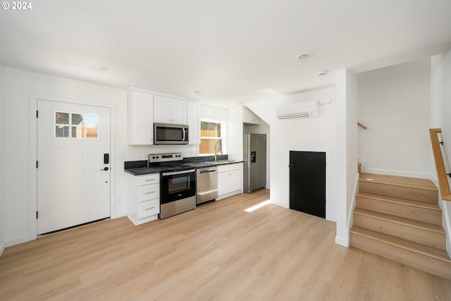6061 NE Simpson St, Portland, OR 97218 - kitchen featuring stainless steel appliances, white cabinets, light wood-style flooring, a wall unit AC, and dark countertops