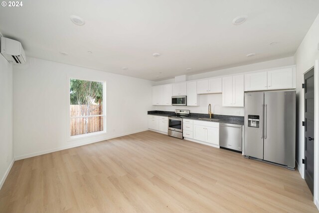 6061 NE Simpson St, Portland, OR 97218 - kitchen featuring stainless steel appliances, dark countertops, an AC wall unit, white cabinetry, and light wood-style floors