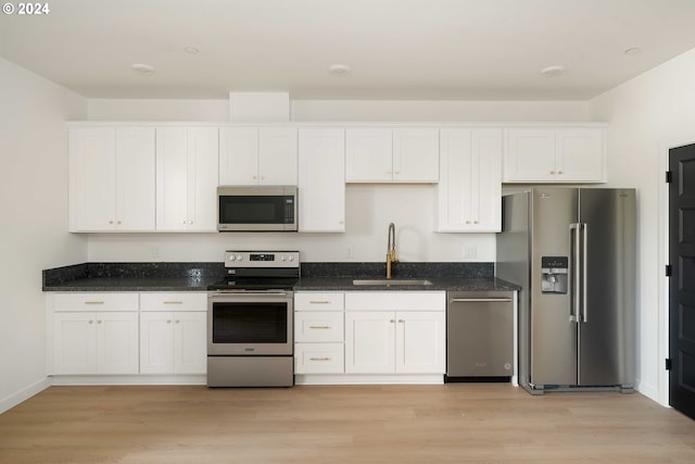 6061 NE Simpson St, Portland, OR 97218 - kitchen with stainless steel appliances, white cabinetry, light wood-style floors, and dark stone countertops