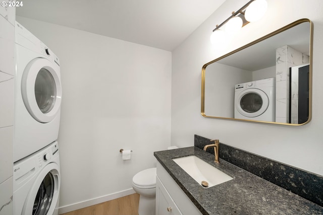 bathroom featuring hardwood / wood-style floors, vanity, toilet, and stacked washing maching and dryer