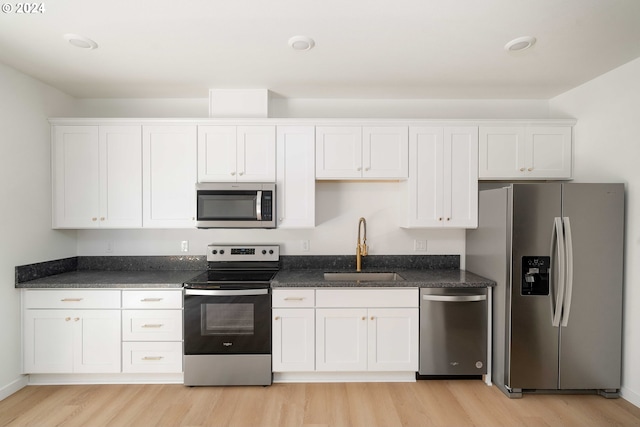 6061 NE Simpson St, Portland, OR 97218 - kitchen featuring appliances with stainless steel finishes, light wood finished floors, white cabinets, and dark stone countertops