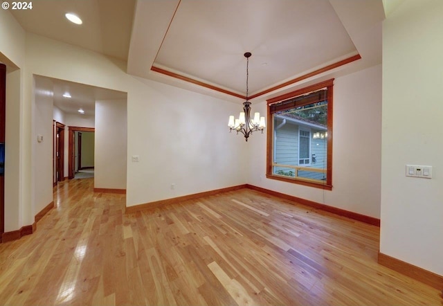 unfurnished dining area featuring light wood-type flooring, a tray ceiling, and a notable chandelier