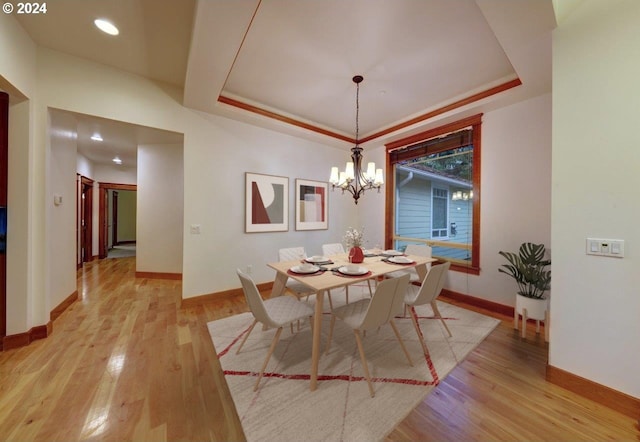 dining space featuring an inviting chandelier, a tray ceiling, and light hardwood / wood-style flooring