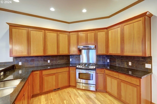 kitchen with dark stone counters, sink, light wood-type flooring, ornamental molding, and stainless steel range with gas stovetop